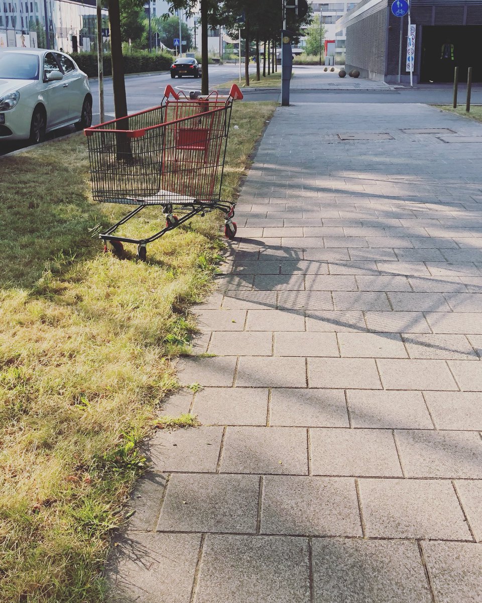 Un caddie de supermarché est abandonné dans une rue du quartier des affaires à Luxembourg, 3 de ses roulettes sont dans un peu d’herbe sur le côté du trottoir