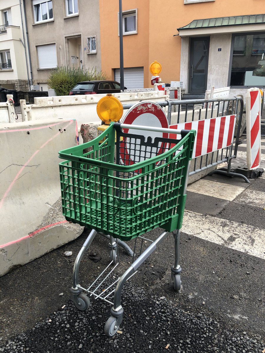 Un caddie en plastique vert devant une zone de travaux dans la rue