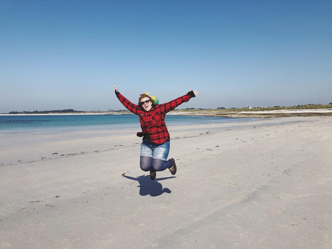 Laurence, sautant de joie sur une plage bretonne, les cheveux au vent